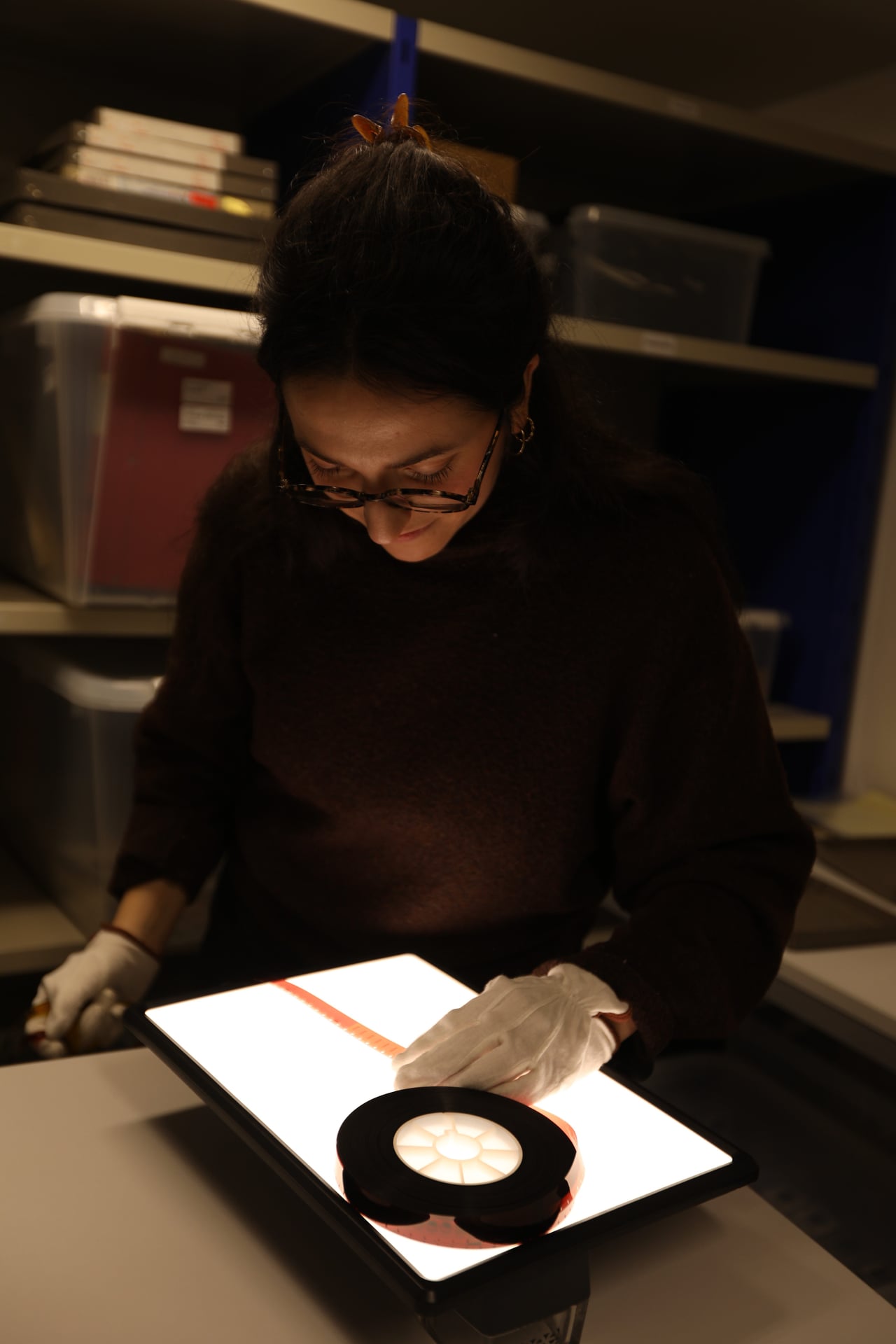 Our archivist Jeanne-Alice inspects a film reel on a lightbox — gloves and careful handling protect the original before any digitisation begins.