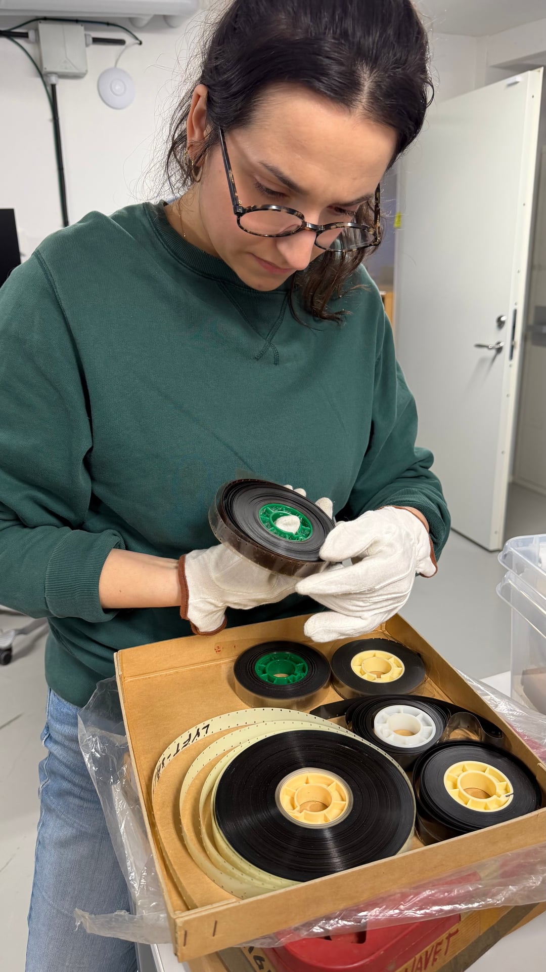 An archivist carefully inspects a film reel from the Börjeson collection. Cotton gloves and methodical handling are standard practice for fragile analogue material.